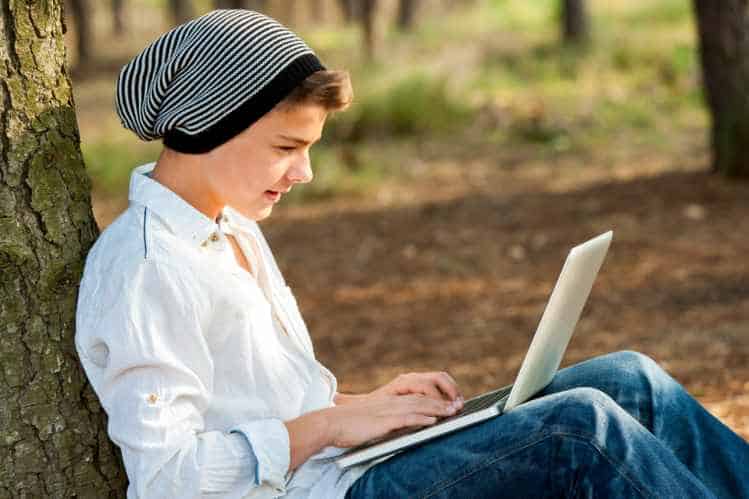 Teen boy socialising on laptop outdoors.